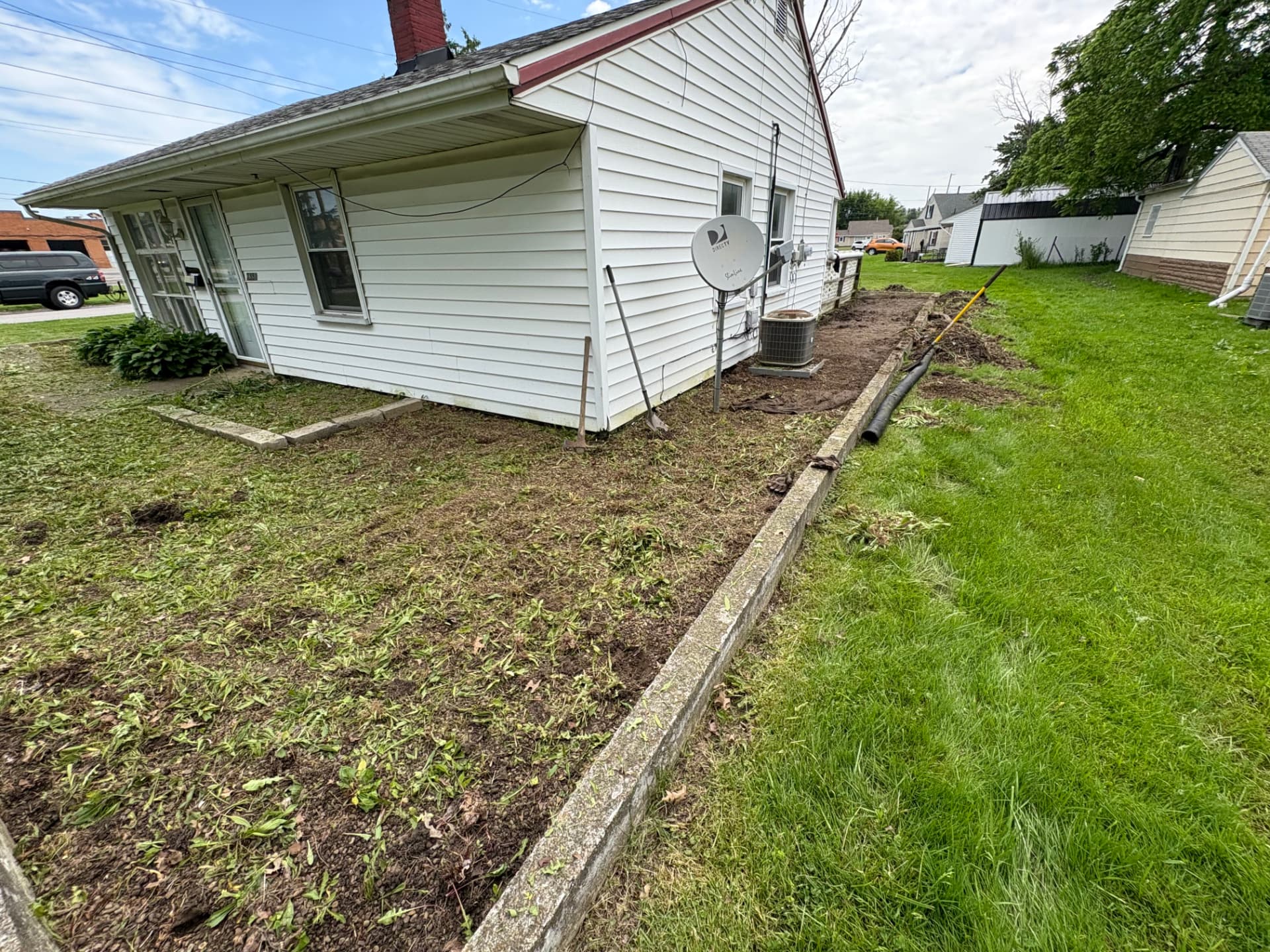 Side yard stripped of overgrowth with soil and edging exposed