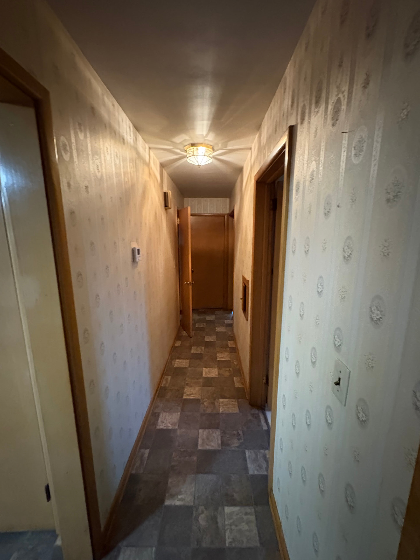 Long hallway with dated wallpaper, worn flooring and yellowed trim before interior painting