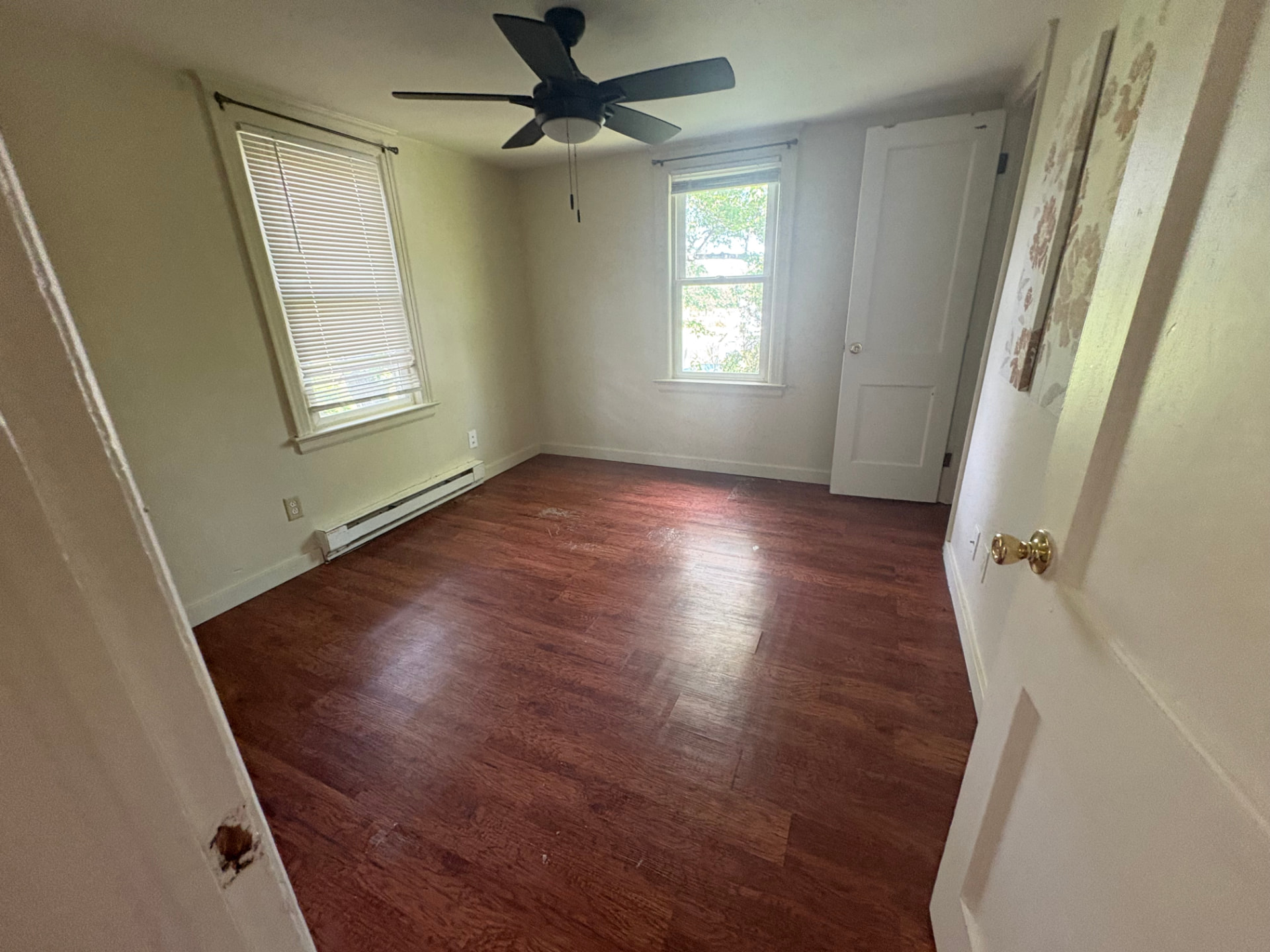 Bedroom with worn hardwood flooring and dated paint before wide plank LVP installation