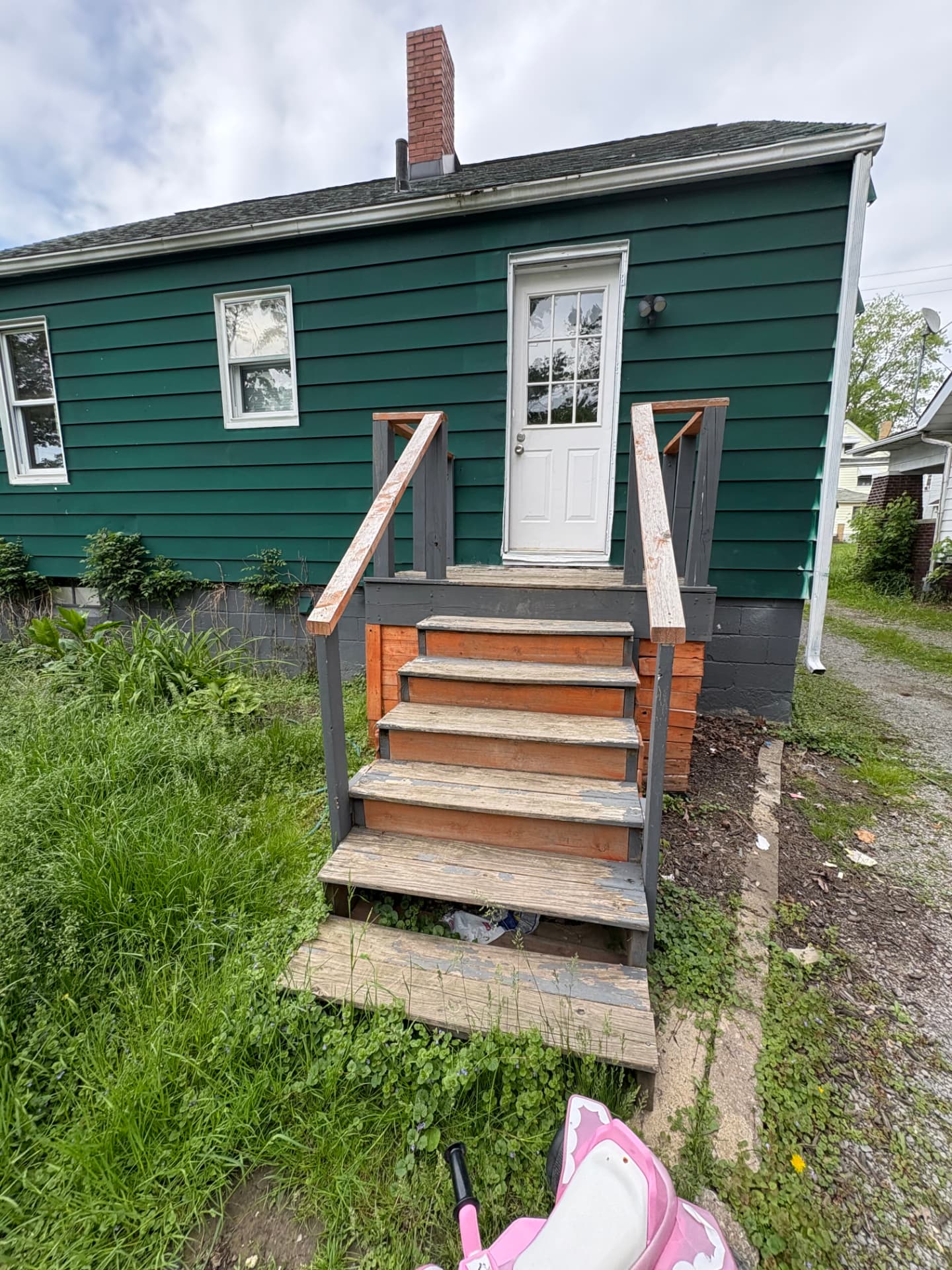 Green house with weathered stairs, overgrown grass and untidy landscaping before paint and cleanup