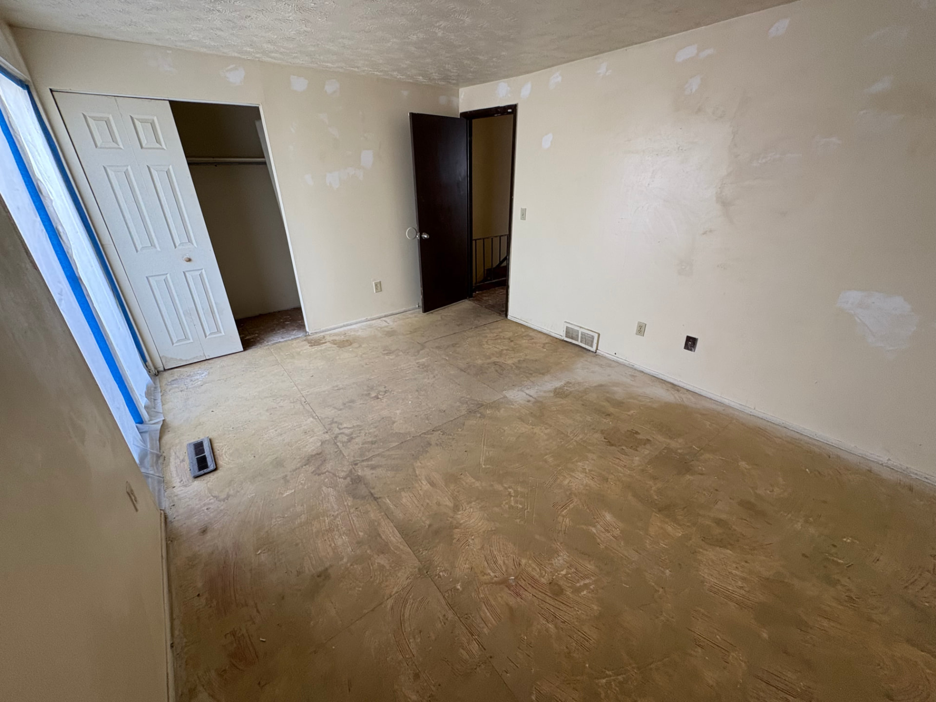Bedroom with old flooring removed, patched walls and exposed subfloor before full remodel