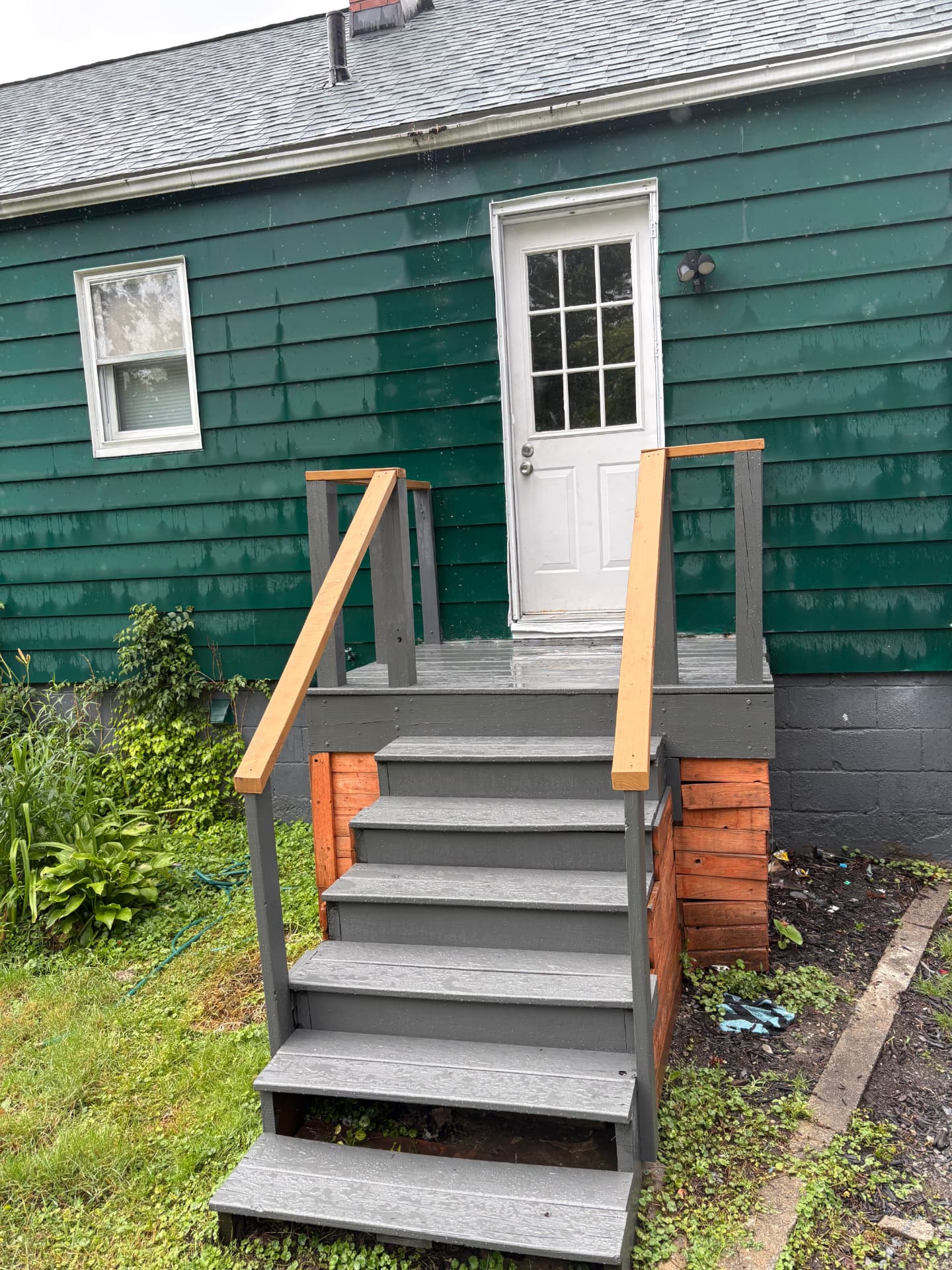 Green house with refreshed gray-painted stairs, tidy landscaping and cleaned surrounding area after paint and general cleanup