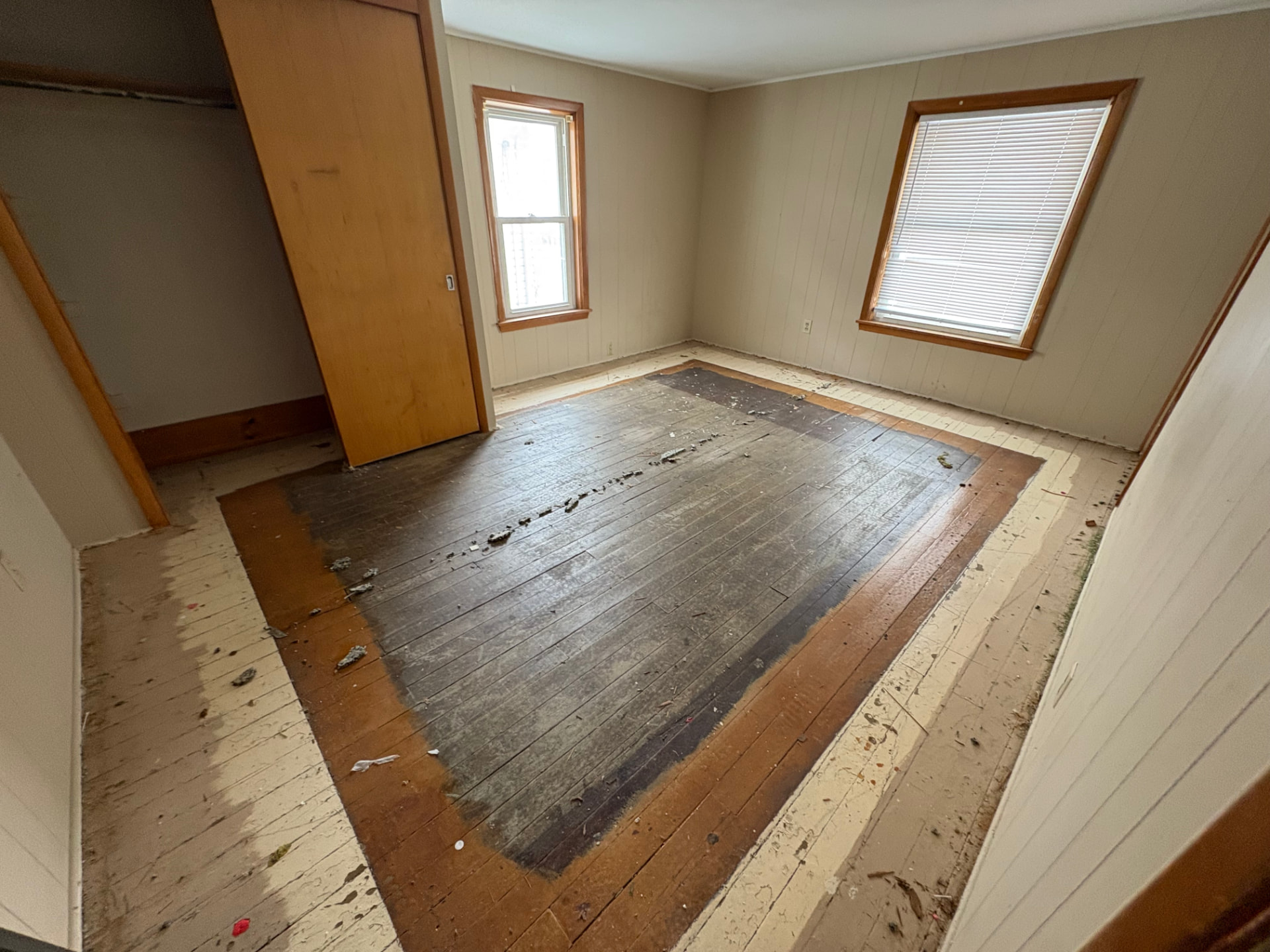 Bedroom with worn, patchy old hardwood and debris before LVP flooring installation